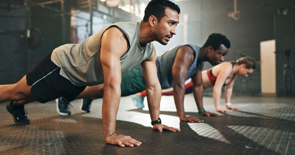 Gym, group fitness and push up exercise for power, sports challenge and muscle on ground. Serious asian man, bodybuilder and performance training on floor with friends, workout class or strong people.